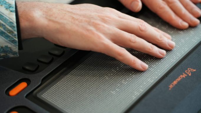photo of adult hands resting atop displayed braille on the Monarch